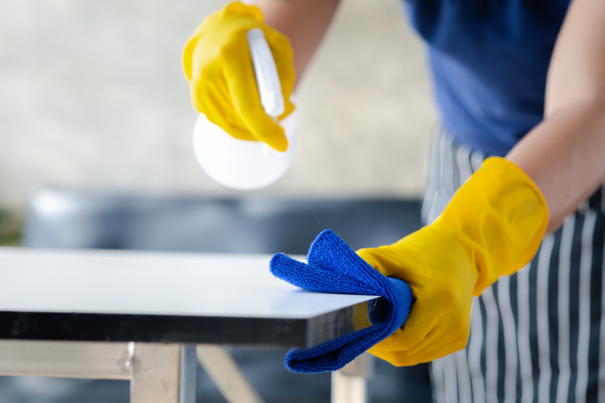 Person cleaning the room, cleaning staff is using cloth and spraying disinfectant.